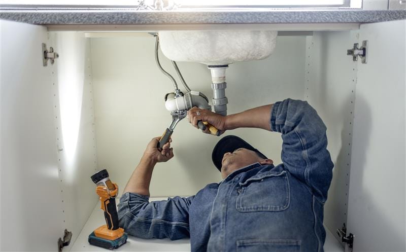 Plumber repairing pipes beneath a bathroom sink in San Rafael